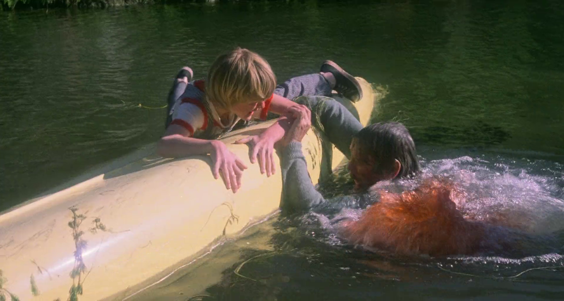 piranha-pirania | film.org.pl Two people clinging to a yellow kayak in a lake; one person's hand reaches toward the other as they struggle in the water.