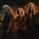 Group of four rugged fantasy warriors with swords and a bow, standing in a smoky, fiery battleground.