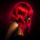 Side profile of a woman with neon pink hair, dripping like paint, wearing a black lace bra against a dark red backdrop.”