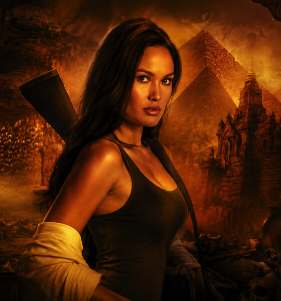 Heroine in a dark tank top stands in a lava-lit cavern with ancient statues, pyramids, and a torch-lit backdrop behind her.
