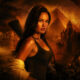 Heroine in a dark tank top stands in a lava-lit cavern with ancient statues, pyramids, and a torch-lit backdrop behind her.