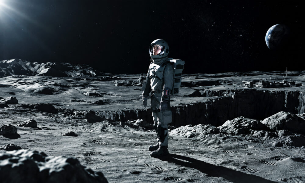 Astronaut standing on the Moon's rocky surface with Earth rising in the dark sky behind him.