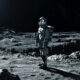 Astronaut standing on the Moon's rocky surface with Earth rising in the dark sky behind him.