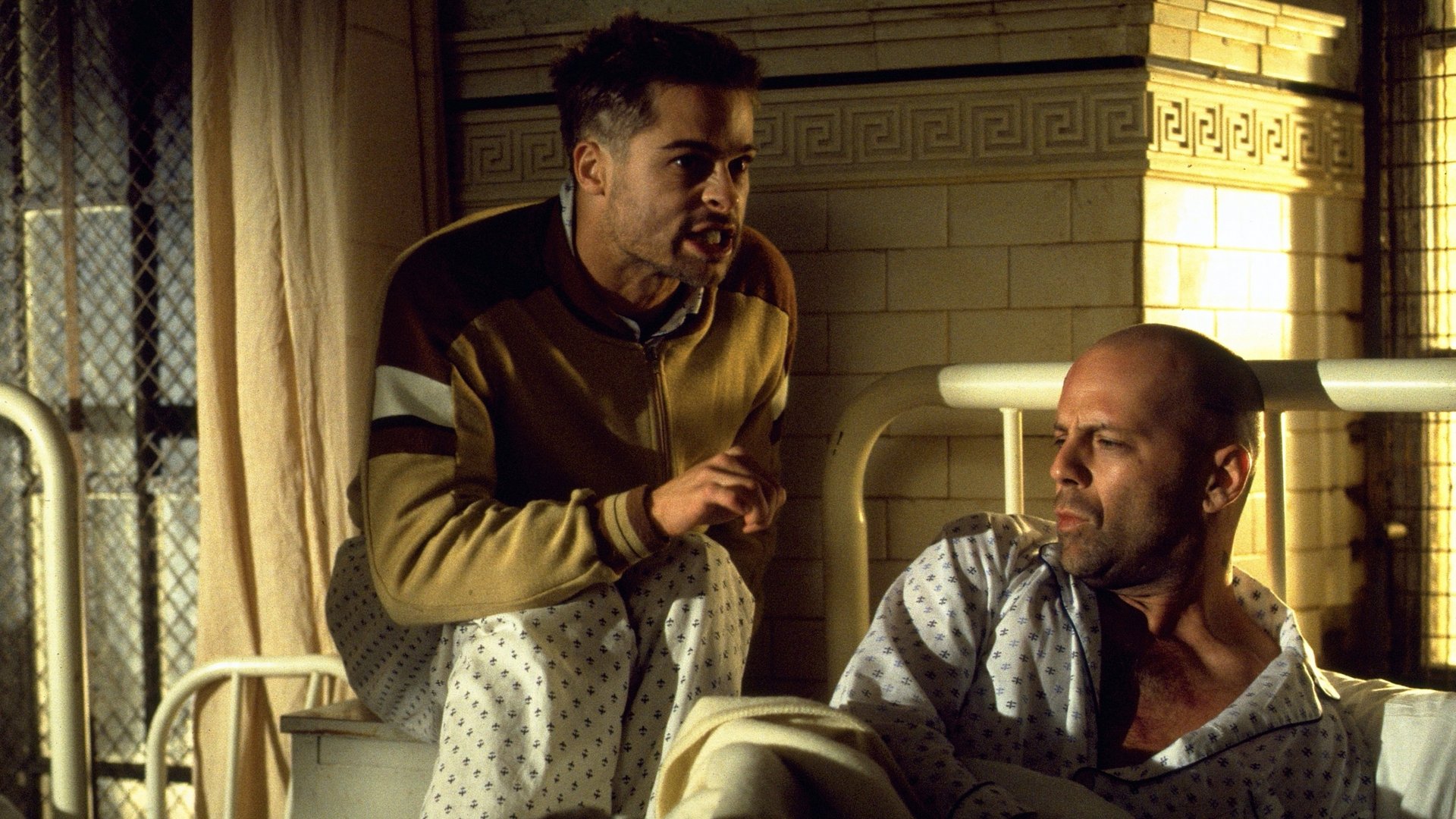 12 małp Twelve Monkeys kadr | film.org.pl Kadr z filmu 12 małp: mężczyzna w brązowej kurtce pochyla się nad łysym mężczyzną w szpitalnym szlafroku na łóżku.