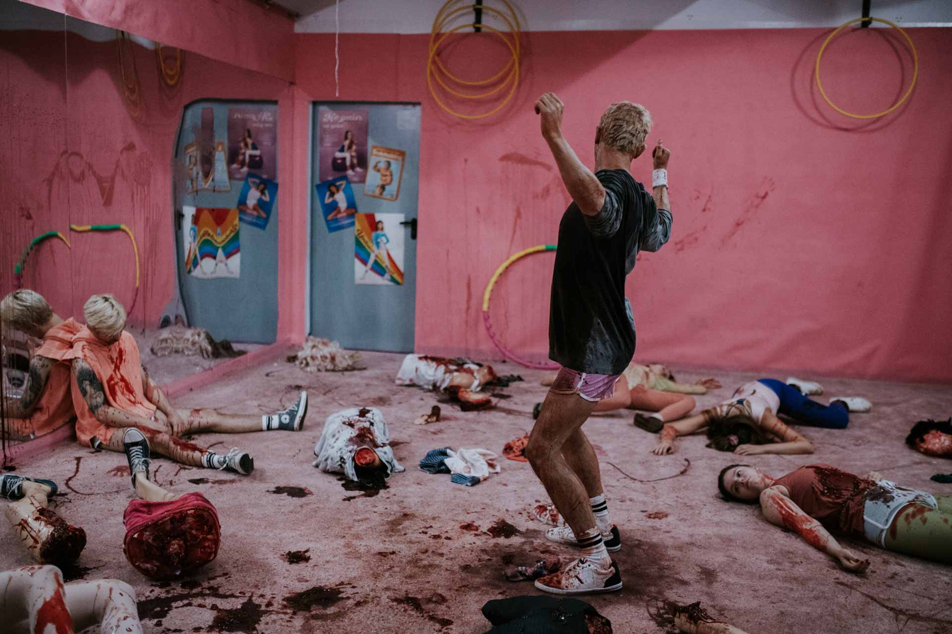 SplatFilmFest | film.org.pl Man in shorts dances in a pink-walled room among several people lying on the floor as props/in a performance setting.