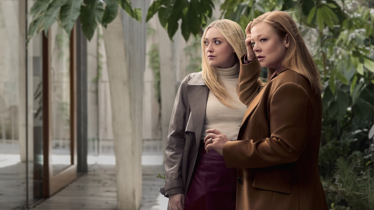 Two women in coats stand outdoors near glass walls, looking off to the side as if discussing something important. all her fault To jej wina