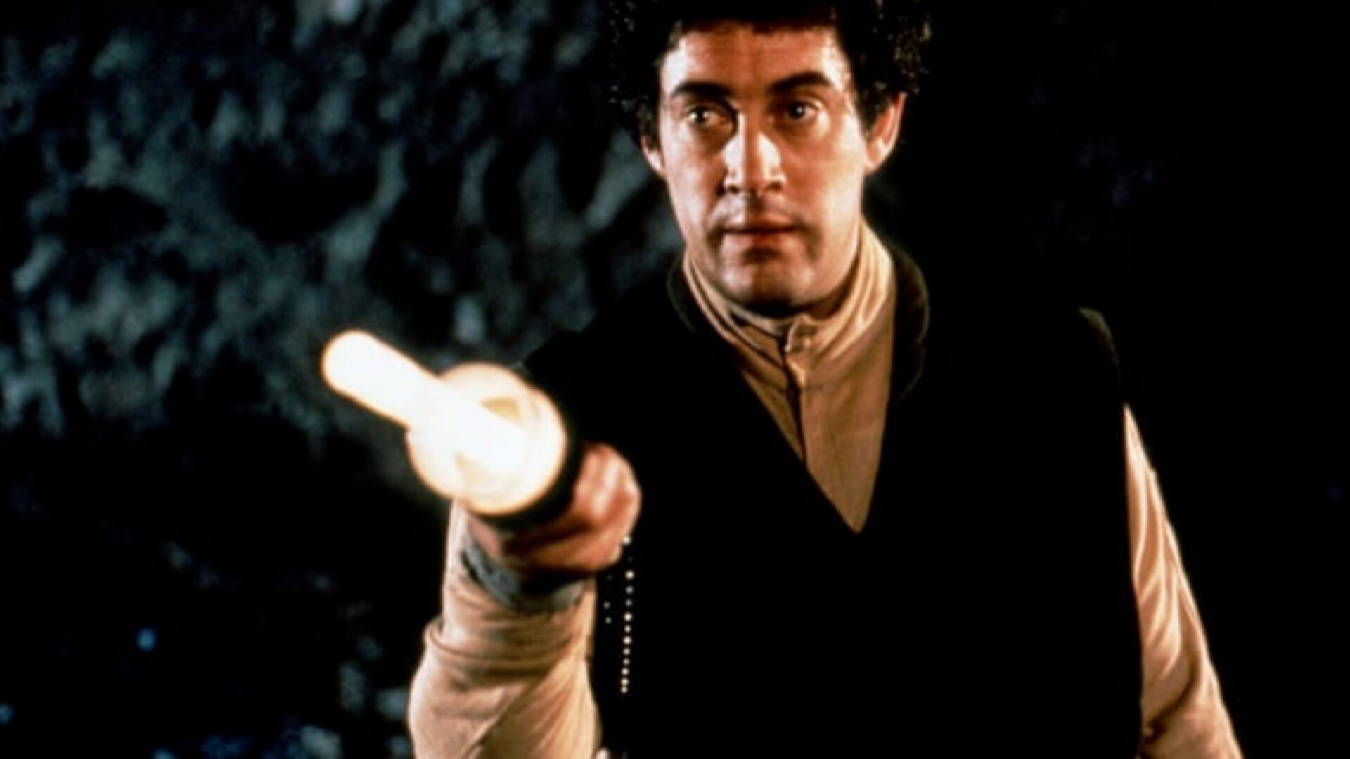 Kadr z serialu Blake's 7: mężczyzna w ciemnej kamizelce i beżowej koszuli wyciąga świecące urządzenie w stronę kamery. Firefly