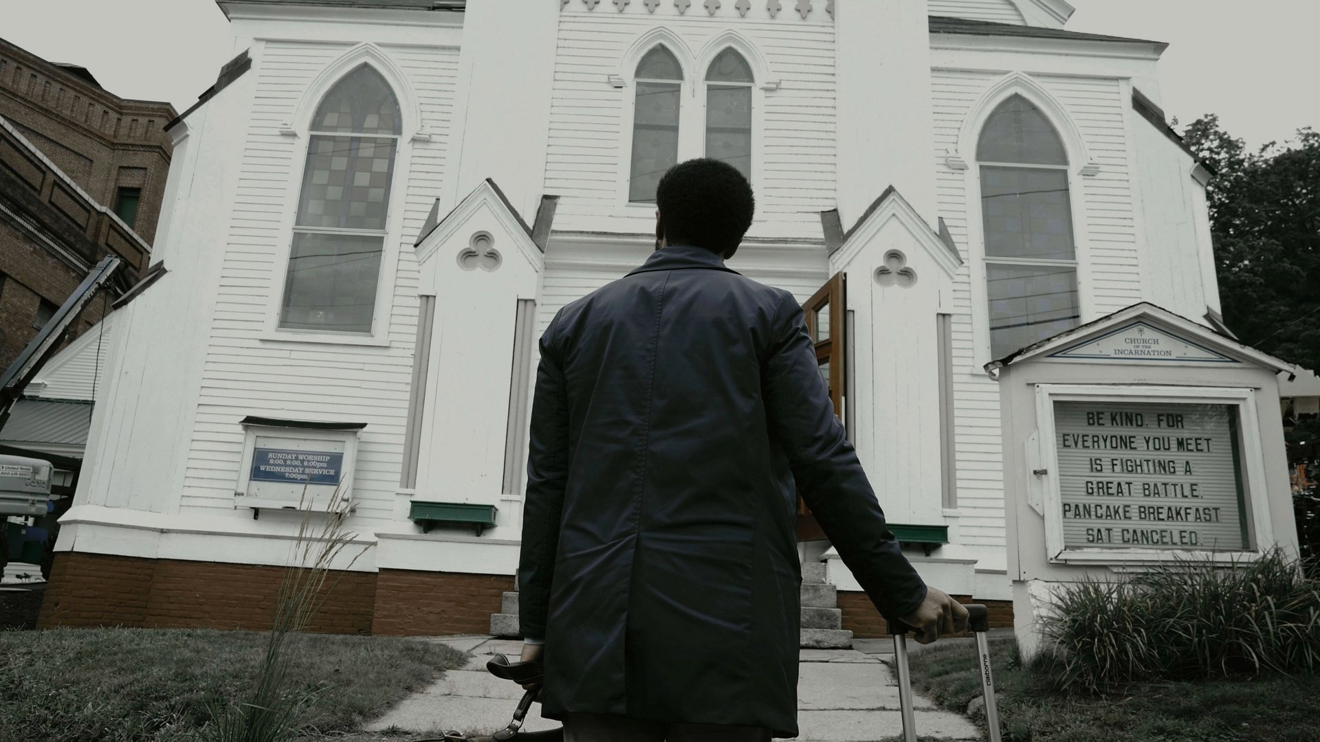 Castle Rock kadr | film.org.pl Kadr z serialu Castle Rock: mężczyzna w ciemnej kurtce idzie od tyłu ku białemu kościołowi z tablicą. TO: Witajcie w Derry