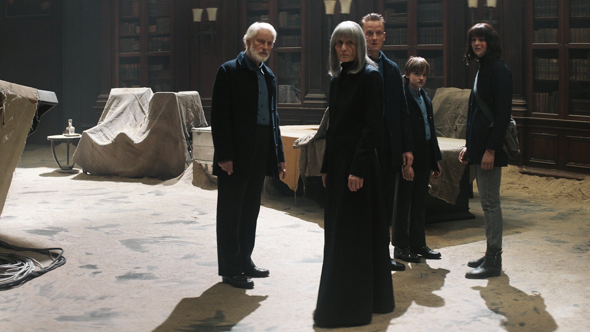 Dark kadr | film.org.pl Kadr z serialu Dark: pięć osób w ciemnych ubraniach stoi w pomieszczeniu z zakrytymi białymi płachtami meblami.