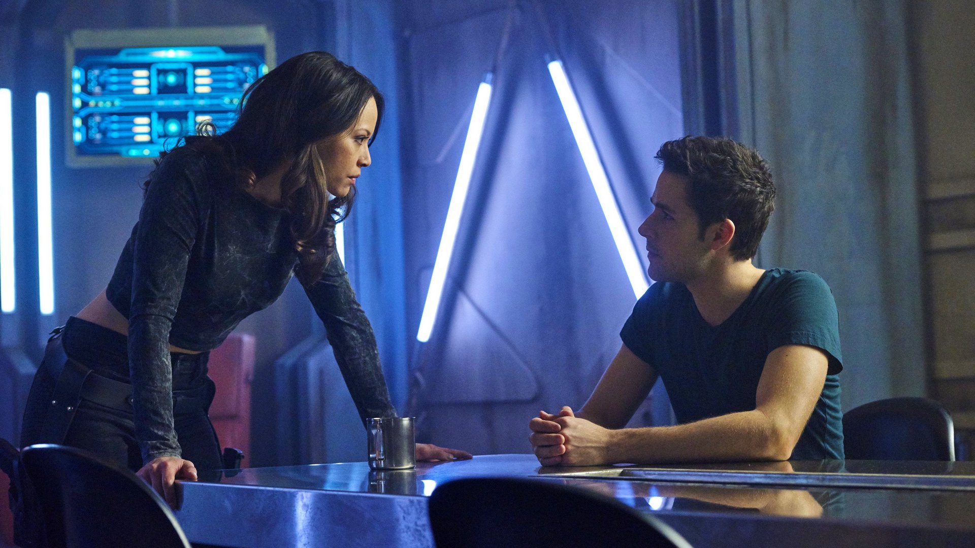 Kadr z serialu Dark Matter: kobieta w czarnym topie pochylona nad stołem rozmawia z siedzącym mężczyzną w futurystycznym wnętrzu. Firefly