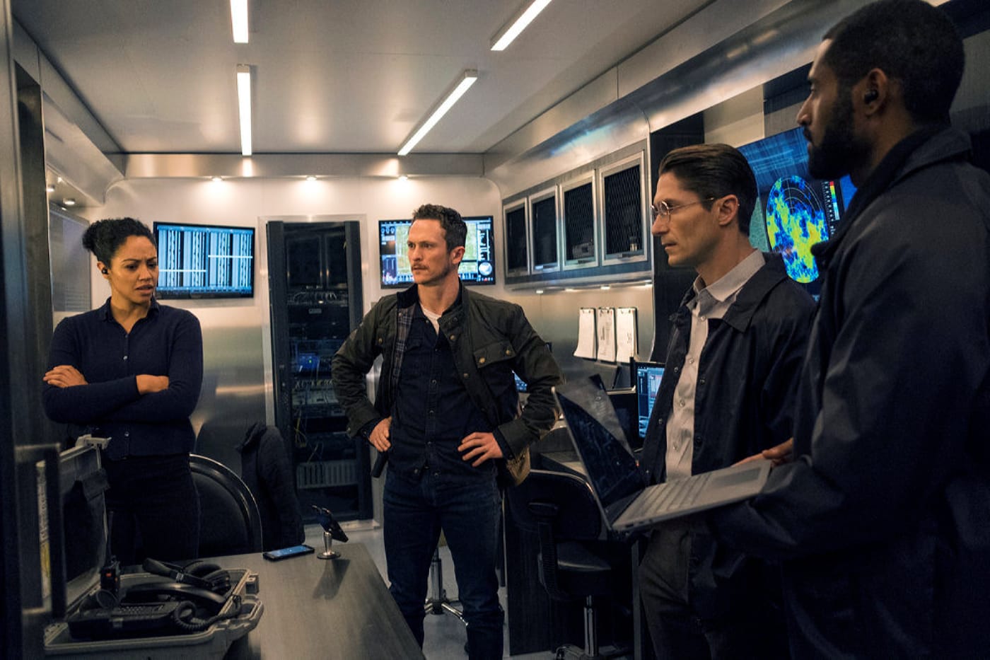 Obcy element | film.org.pl Four analysts in a high-tech control room discussing near workstations with multiple monitors and a radar-style display in the background.