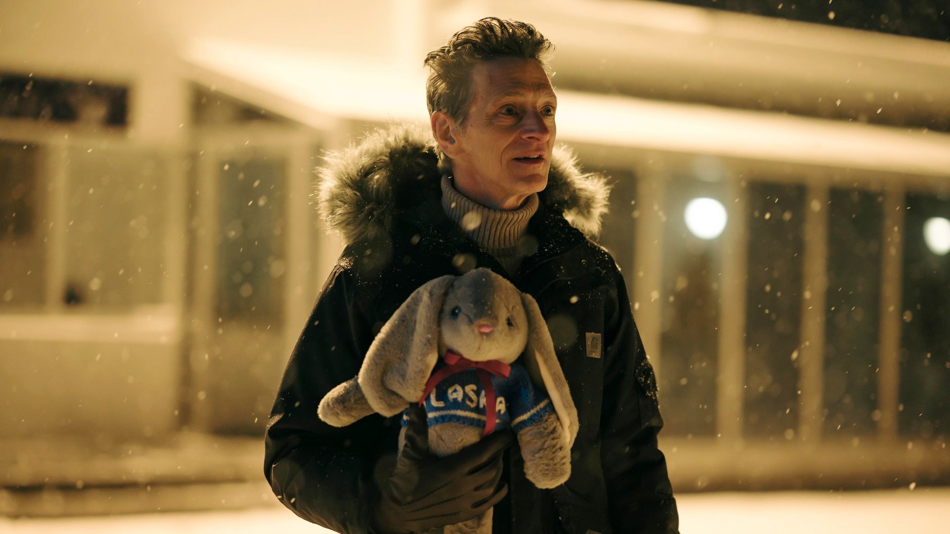 Detektyw True Detective kadr | film.org.pl mężczyzna w ciemnej kurtce z futrzanym kapturem trzyma pluszowego królika w swetrze podczas śnieżycy nocą.