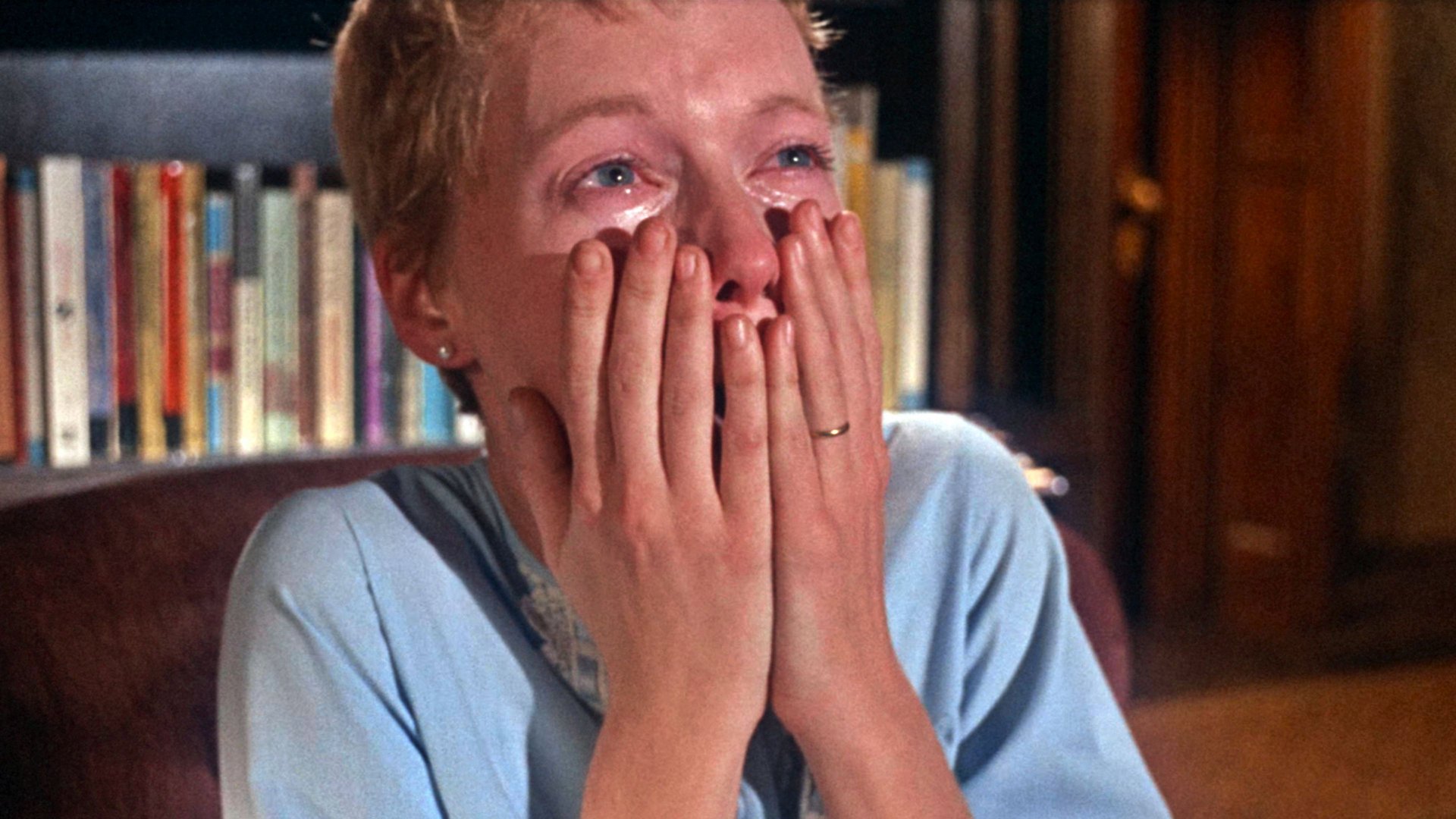 Dziecko Rosemary Rosemarys Baby kadr | film.org.pl Kadr z filmu Dziecko Rosemary: kobieta w jasnoniebieskiej bluzce z krótkimi jasnymi włosami zakrywa dłońmi usta i płacze.