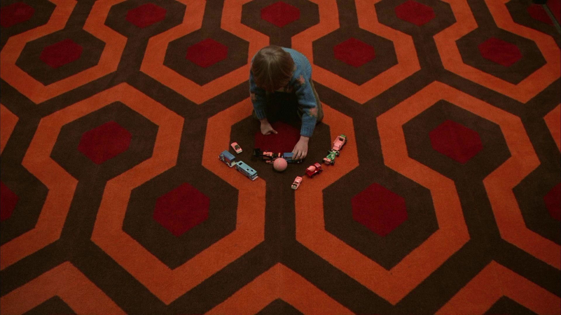 Lśnienie The Shining kadr | film.org.pl Kadr z filmu Lśnienie: dziecko z góry bawi się zabawkowymi autami i piłką na dywanie w geometryczny wzór.