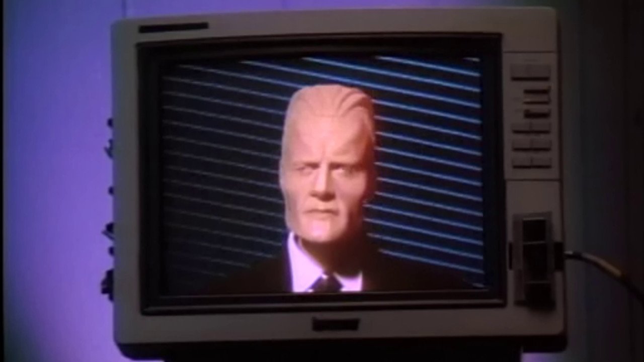 Kadr z serialu Max Headroom: stylizowana cyfrowa głowa mężczyzny w garniturze na ekranie starego telewizora z niebieskimi pasami