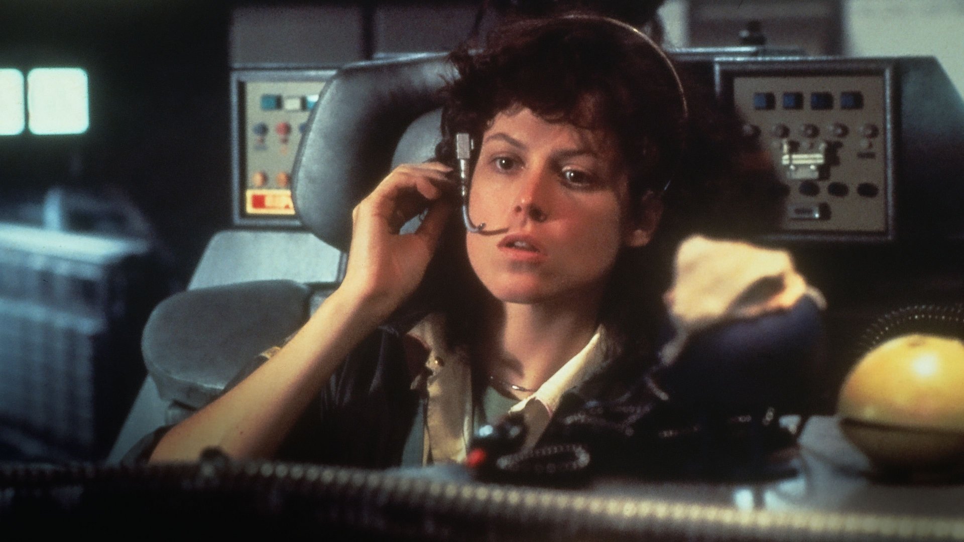Obcy 8 pasażer Nostromo Alien kadr | film.org.pl Kadr z filmu Obcy: 8 pasażer Nostromo: kobieta z mikrofonem przy uchu siedzi na fotelu przed panelami sterowania statku