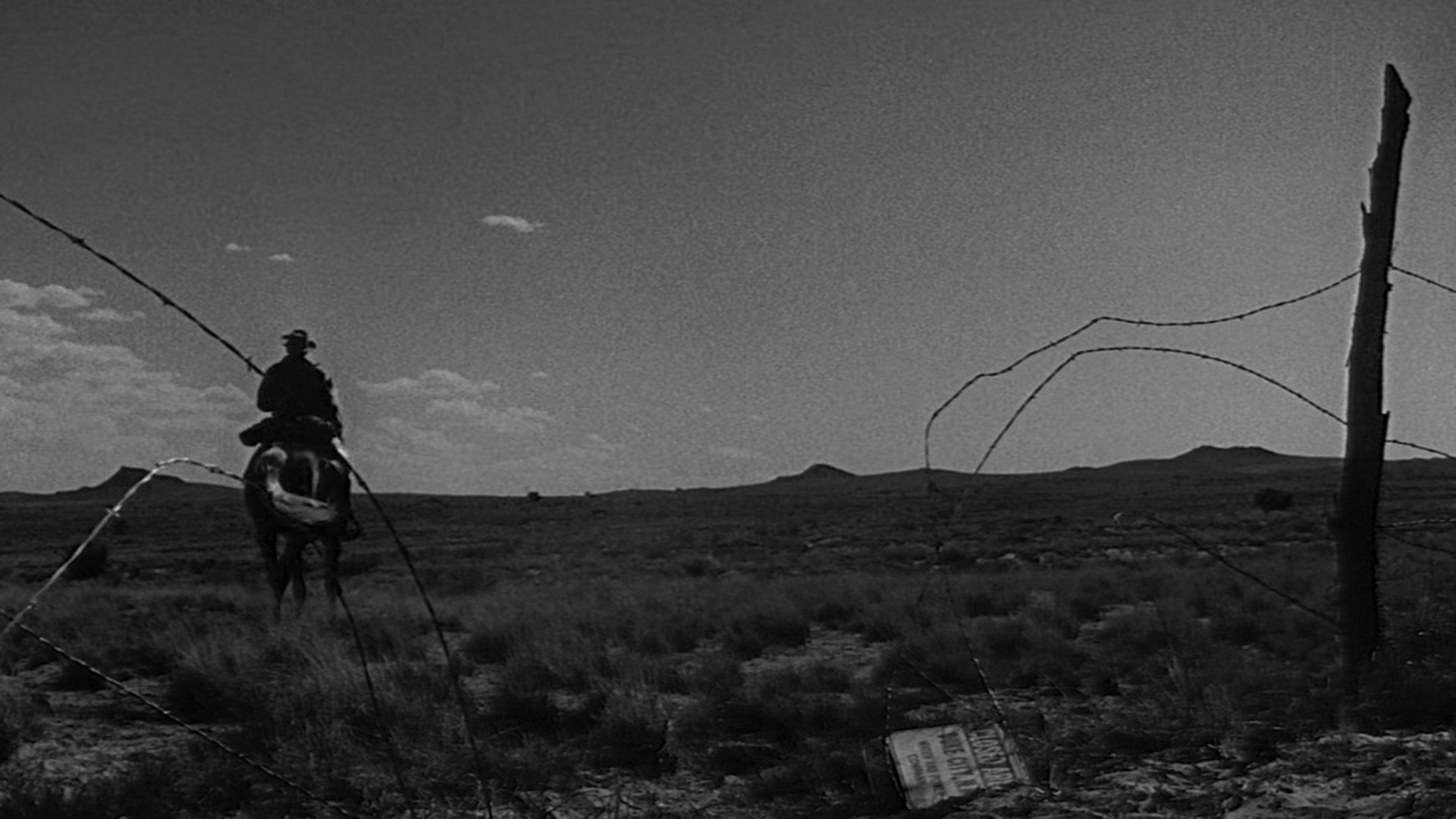 Ostatni kowboj Lonely are the Brave kadr | film.org.pl Kadr z filmu Ostatni kowboj: jeździec na koniu w kapeluszu jedzie przez suchy pustynny krajobraz przy drucianym ogrodzeniu. Rewizjonistyczny western
