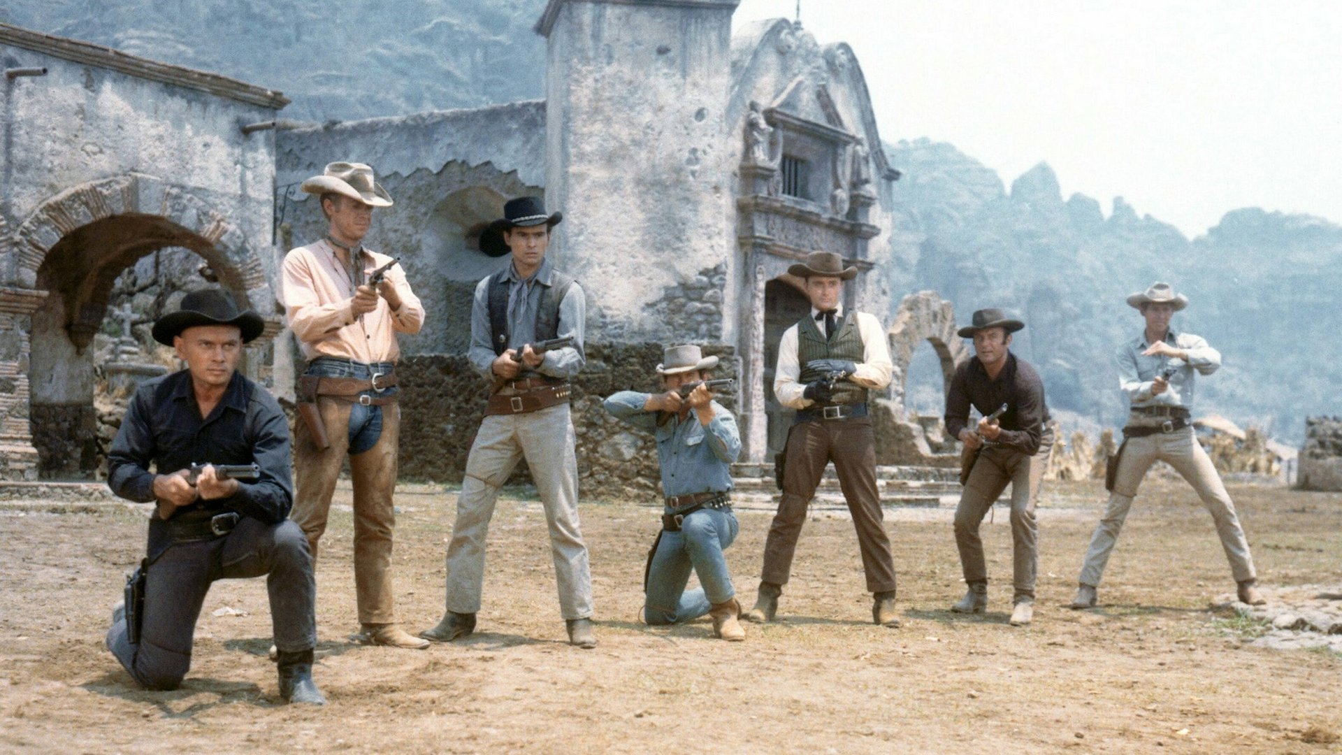 Siedmiu Wspaniałych The Magnificent Seven kadr | film.org.pl Kadr z filmu Siedmiu Wspaniałych: siedmiu uzbrojonych kowbojów stoi i klęka na placu przed ruiną meksykańskiej misji. Bitwa wśród gwiazd