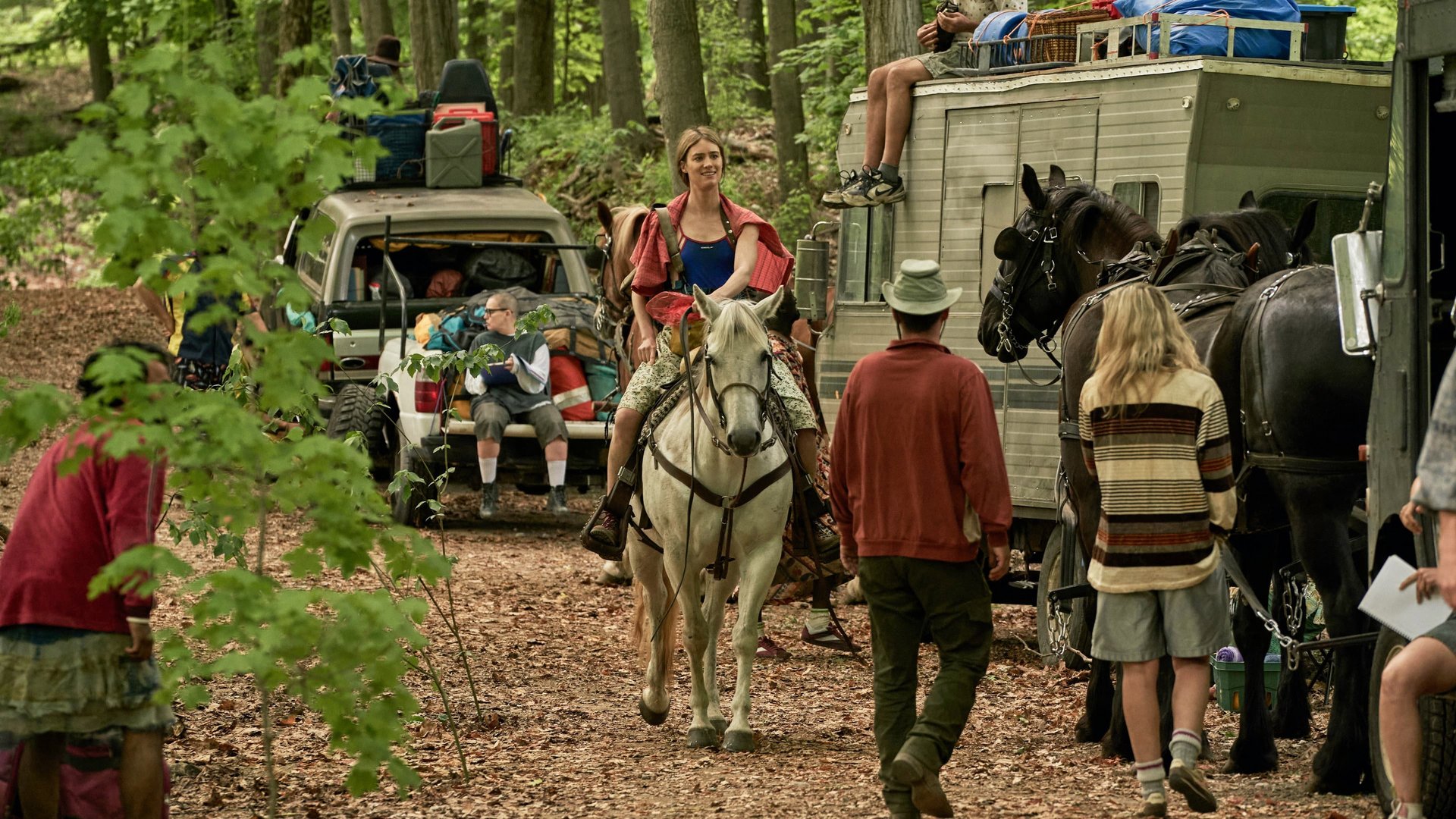 Stacja Jedenasta Station Eleven kadr | film.org.pl Kadr z serialu Stacja Jedenasta: kobieta jedzie na białym koniu w lesie, obok wóz konny i ludzie z bagażem. sci-fi