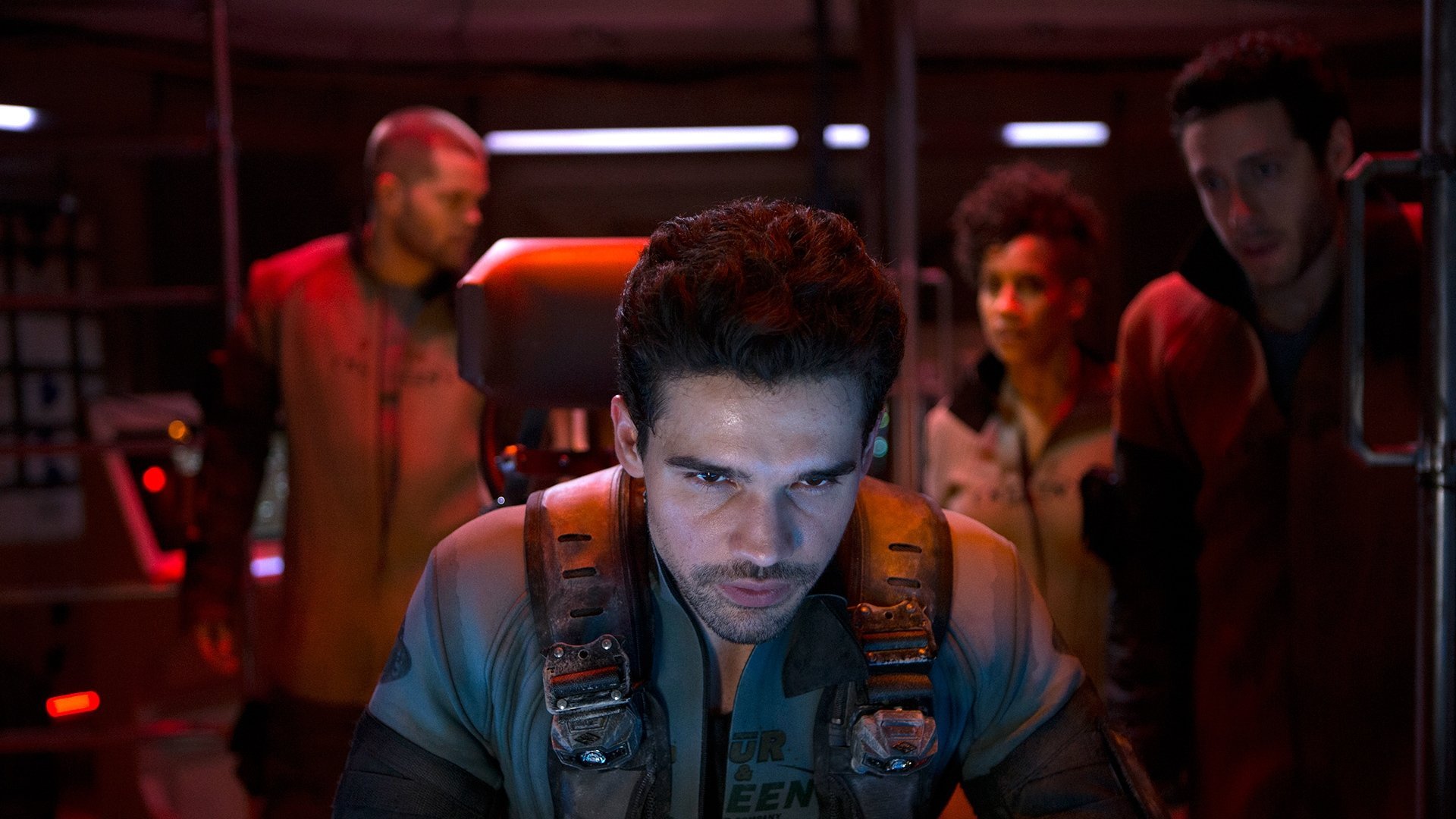 Kadr z serialu The Expanse: mężczyzna w szarym kombinezonie na pierwszym planie, za nim postacie w czerwonym świetle statku.