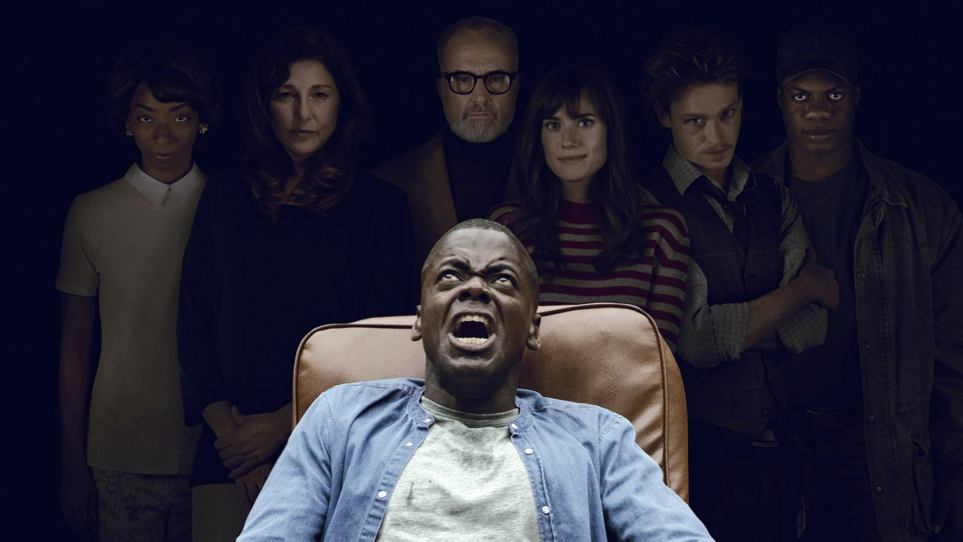 Uciekaj Get Out kadr | film.org.pl Kadr z filmu Uciekaj!: mężczyzna w fotelu z przerażoną miną, za nim stoi grupa ludzi w ciemnym tle.
