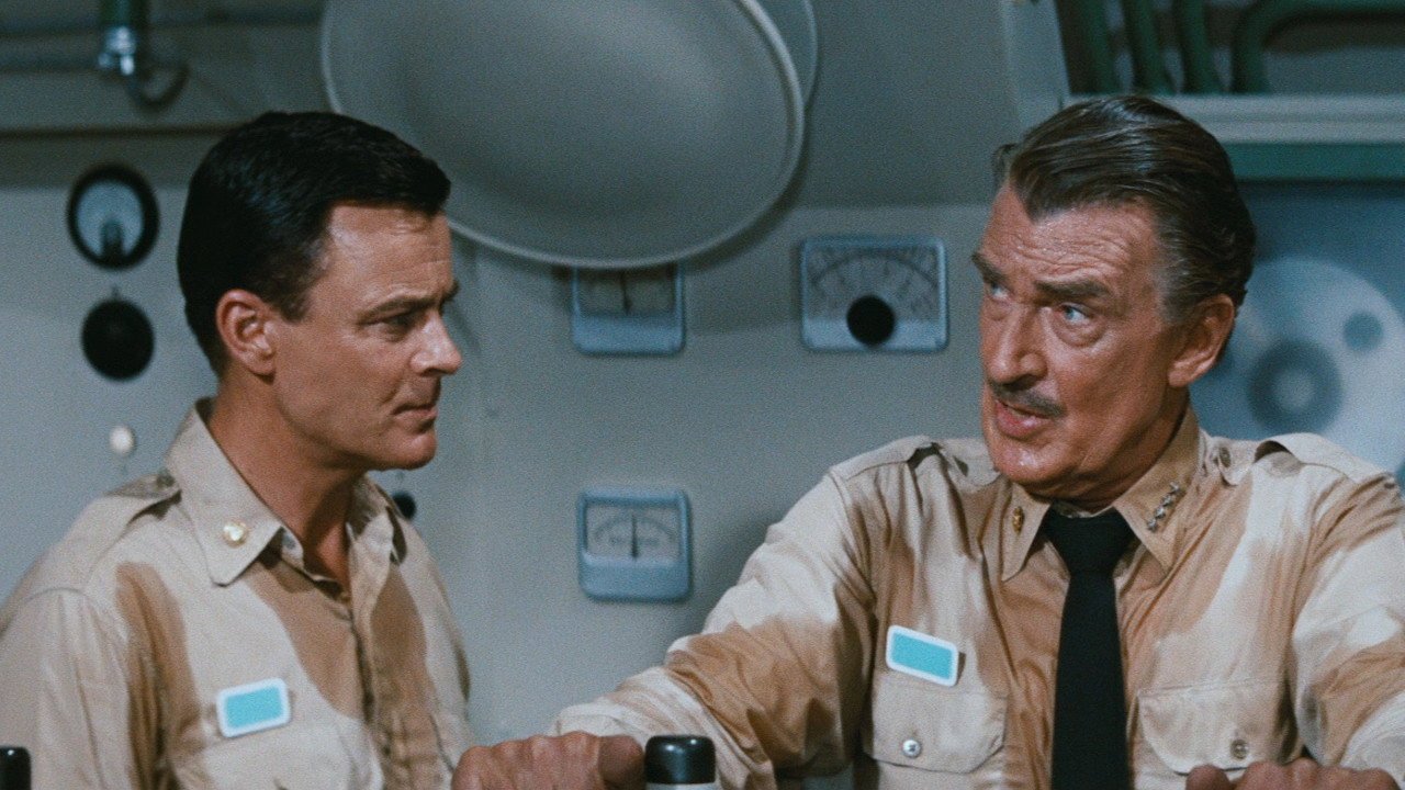 Kadr z filmu Voyage to the Bottom of the Sea: dwaj mężczyźni w beżowych mundurach siedzą przy urządzeniach pokładowych, jeden patrzy w bok, drugi z wąsem i krawatem mówi.