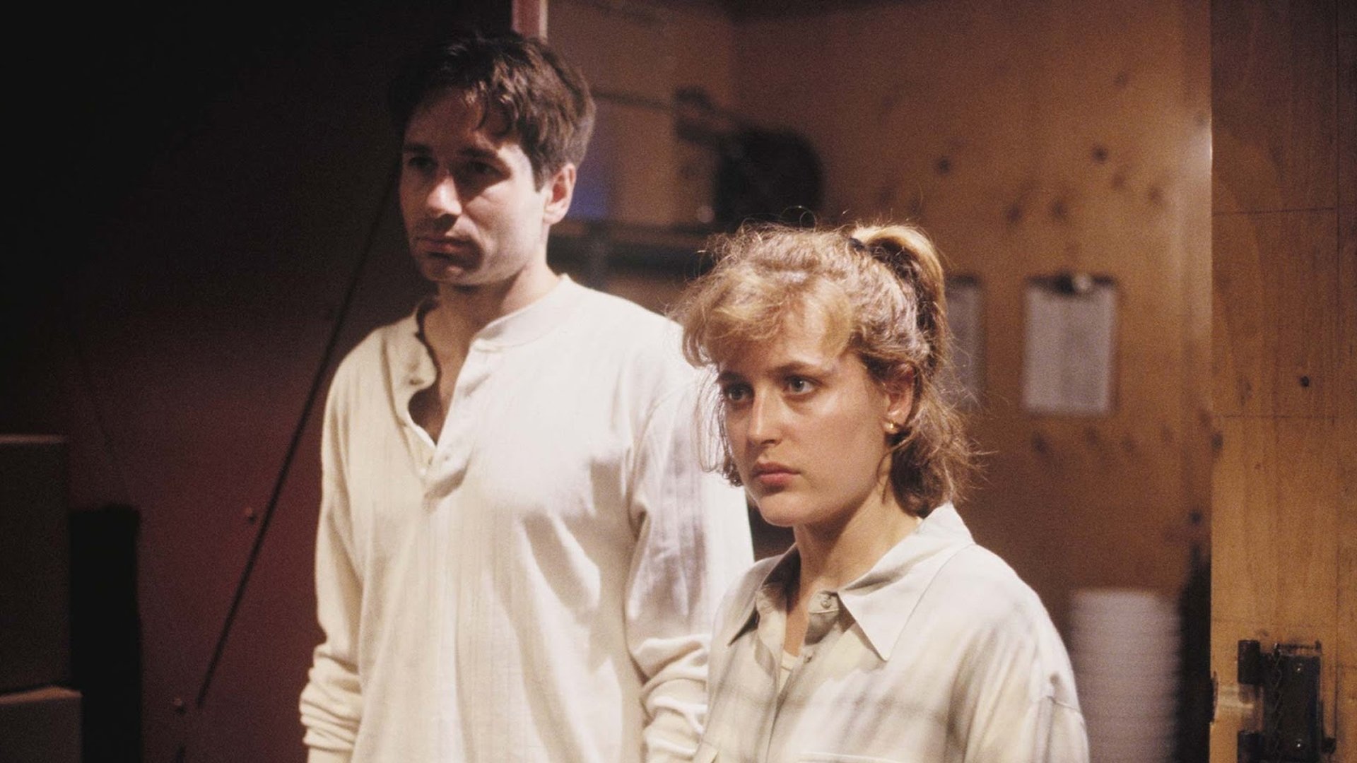 Z Archiwum X The X-Files kadr | film.org.pl Kadr z odcinka Lód: mężczyzna w kremowej koszuli i kobieta z kucykiem stoją obok siebie w drewnianym pomieszczeniu. Z Archiwum X