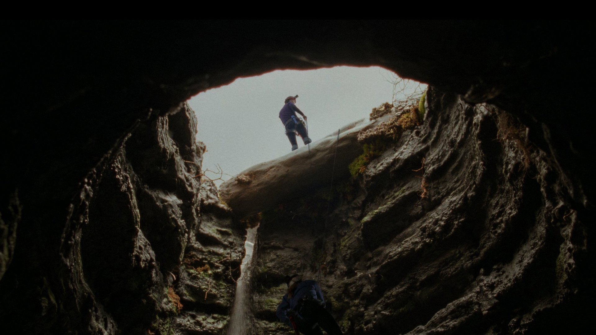 Zejście The Descent kadr | film.org.pl Kadr z filmu Zejście: postać stojąca na krawędzi otworu w skalnej jaskini, widziana od dołu, z jasnym światłem nad nią.